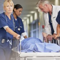 Doctor and nurses wheeling patient in gurney down hospital corridor