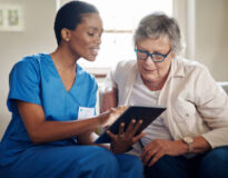 Shot of a senior woman using a digital tablet with a nurse on the sofa at home