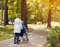 Hospice nurse helping elderly man on wheelchair outdoor